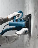 Een persoon met veiligheidsuitrusting bedient een muurfrees om een groef in beton te frezen.