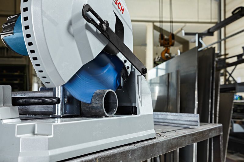 Een metaalafkortzaag zaagt door een ronde metalen buis in een industriële werkplaats.