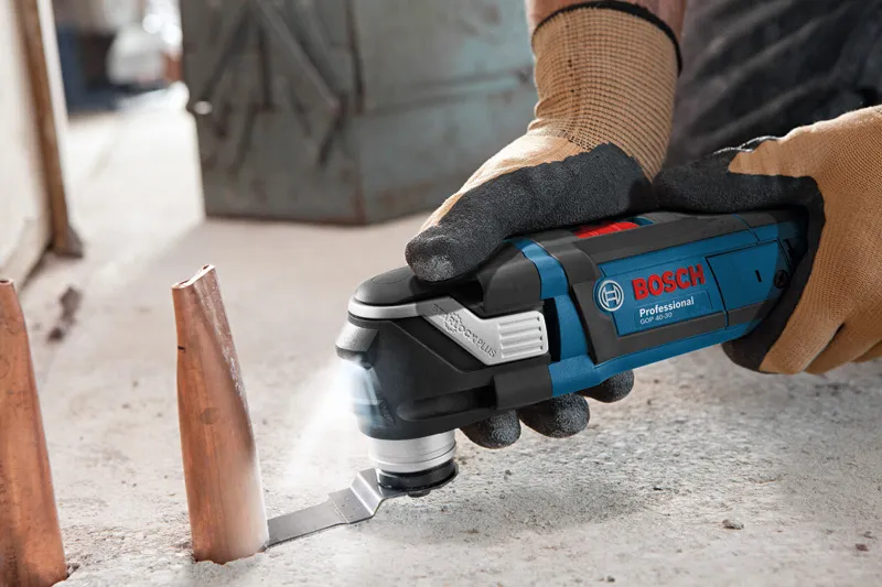 Een persoon die veiligheidsmateriaal draagt, gebruikt een multi-cutter om een metalen pijp op een betonnen vloer door te snijden.