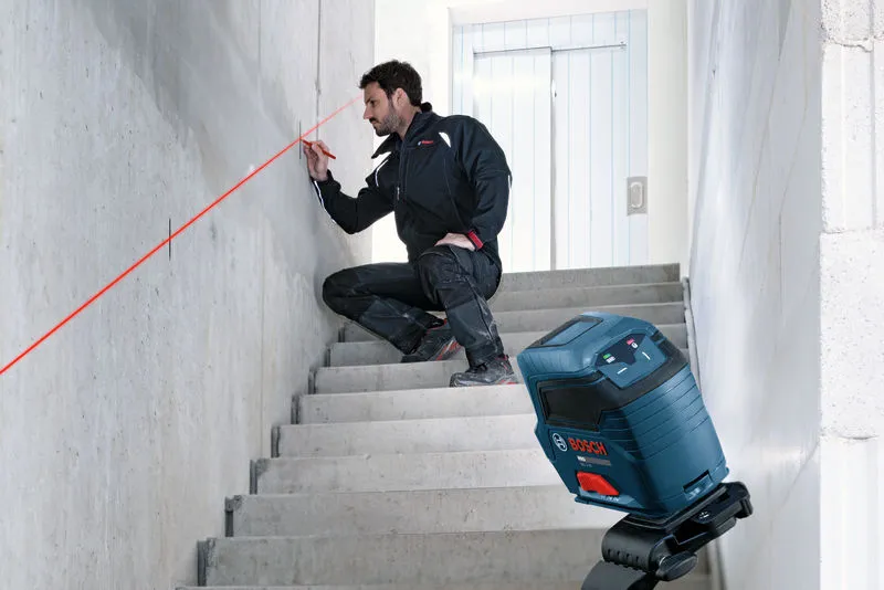 Een persoon tekent hulplijnen op een muur met behulp van een laserwaterpas op een trap.