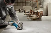 Een persoon met veiligheidsuitrusting zaagt een plaat met een haakse slijper in een werkplaats.