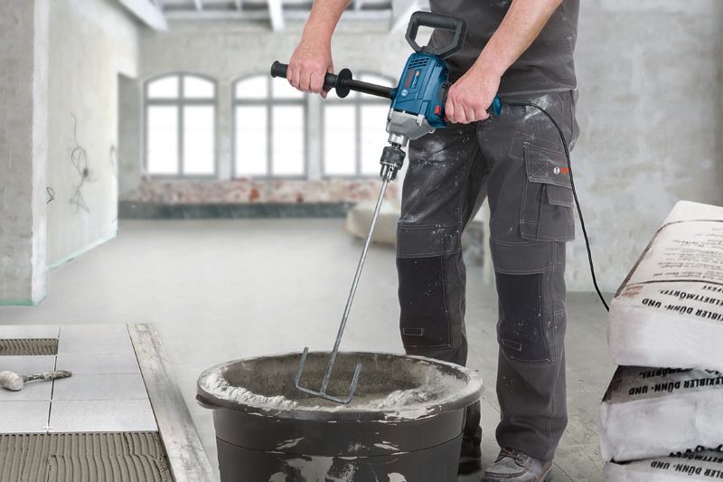 Een persoon die veiligheidsmateriaal draagt, mengt cement in een emmer met behulp van een elektrische mixer.