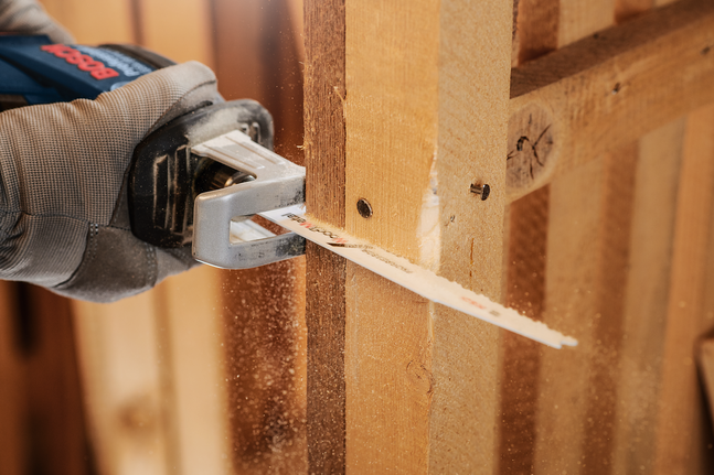 Een persoon met veiligheidsuitrusting zaagt een houten balk door met een reciprozaag.