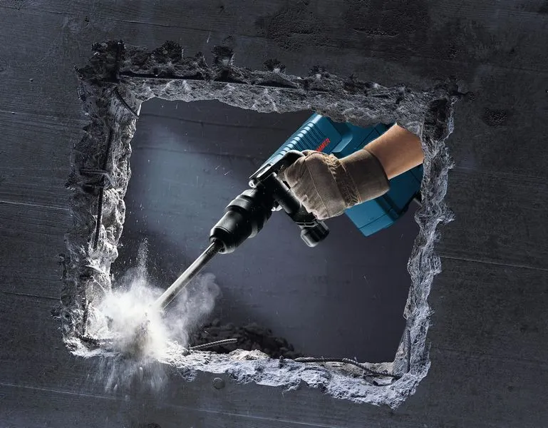 Een persoon die veiligheidsuitrusting draagt, gebruikt een breekhamer om een betonnen muur te breken.