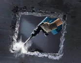 Een persoon die veiligheidsuitrusting draagt, gebruikt een breekhamer om een betonnen muur te breken.