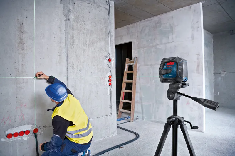 Een persoon die veiligheidsuitrusting draagt, markeert een muur met behulp van een laserwaterpas.