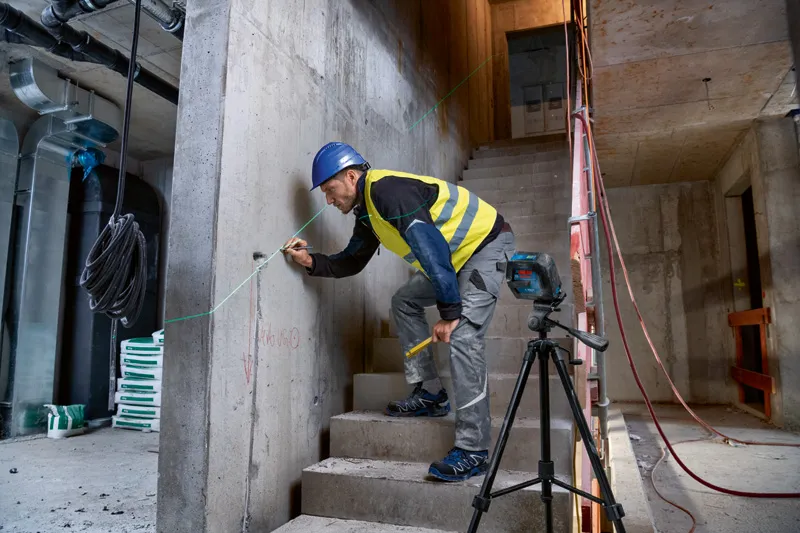 Een persoon die veiligheidsuitrusting draagt, markeert een betonnen muur met behulp van een laserwaterpas.