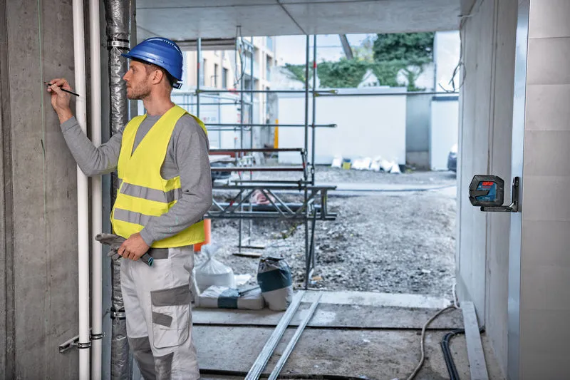 Een persoon die veiligheidsuitrusting draagt, markeert een muur met behulp van een laserwaterpas.