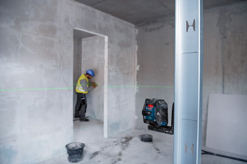 Een persoon met veiligheidsuitrusting markeert een muur met behulp van een groene laserwaterpas.