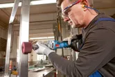 Een persoon die veiligheidsuitrusting draagt, gebruikt een snoerloze rechte slijper op een stalen balk.