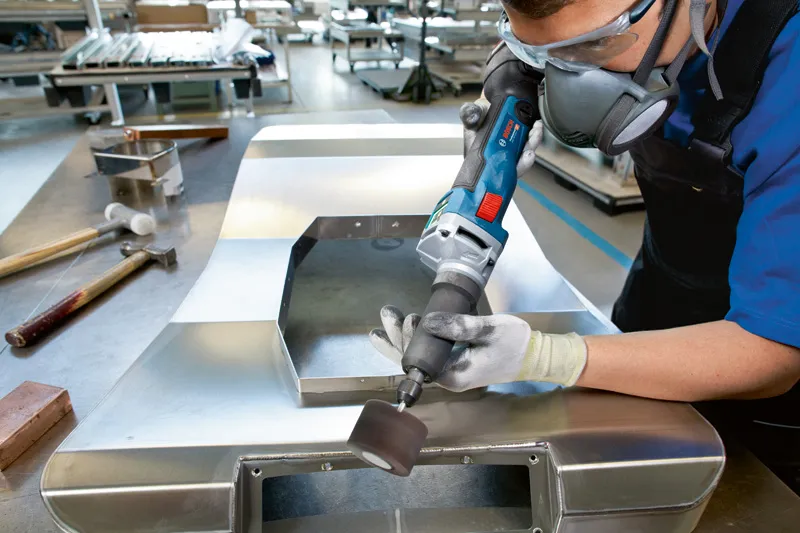 Een persoon met veiligheidsuitrusting slijpt een metalen plaat met een snoerloze rechte slijper.