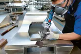 Een persoon met veiligheidsuitrusting slijpt een metalen plaat met een snoerloze rechte slijper.