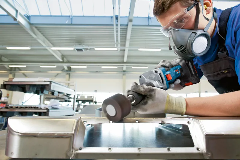 Een persoon die veiligheidsuitrusting draagt, slijpt een metalen oppervlak met een snoerloze rechte slijper.
