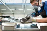 Een persoon die veiligheidsuitrusting draagt, slijpt een metalen oppervlak met een snoerloze rechte slijper.