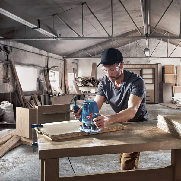 Een persoon die veiligheidsuitrusting draagt, gebruikt een freesmachine om hout te bewerken in een werkplaats.