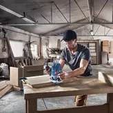 Een persoon die veiligheidsuitrusting draagt, gebruikt een freesmachine om hout te bewerken in een werkplaats.