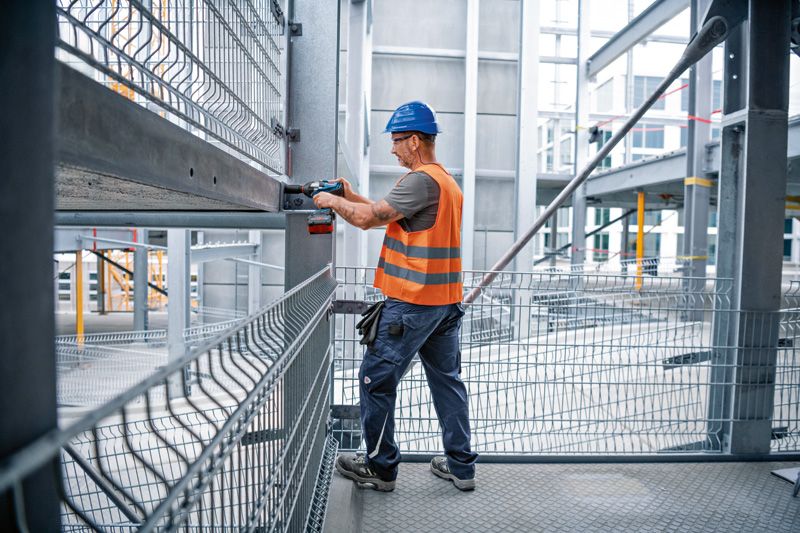 Een persoon die veiligheidsuitrusting draagt, gebruikt een slagsleutel om een stalen balk op een bouwplaats te bewerken.