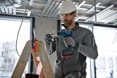 Een persoon die veiligheidsuitrusting draagt, gebruikt een draadloos gereedschap om elektrische draden te strippen.