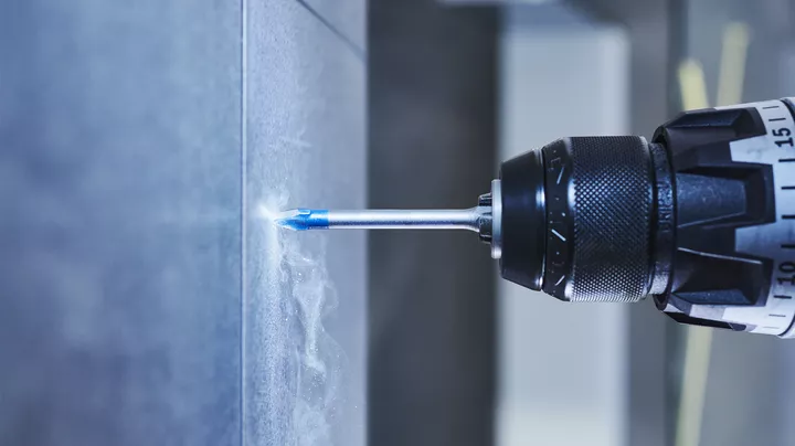 Een boormachine maakt een gat in een betegelde muur.