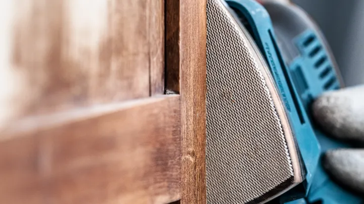 Persoon met veiligheidsuitrusting schuurt de rand van een houten deur.