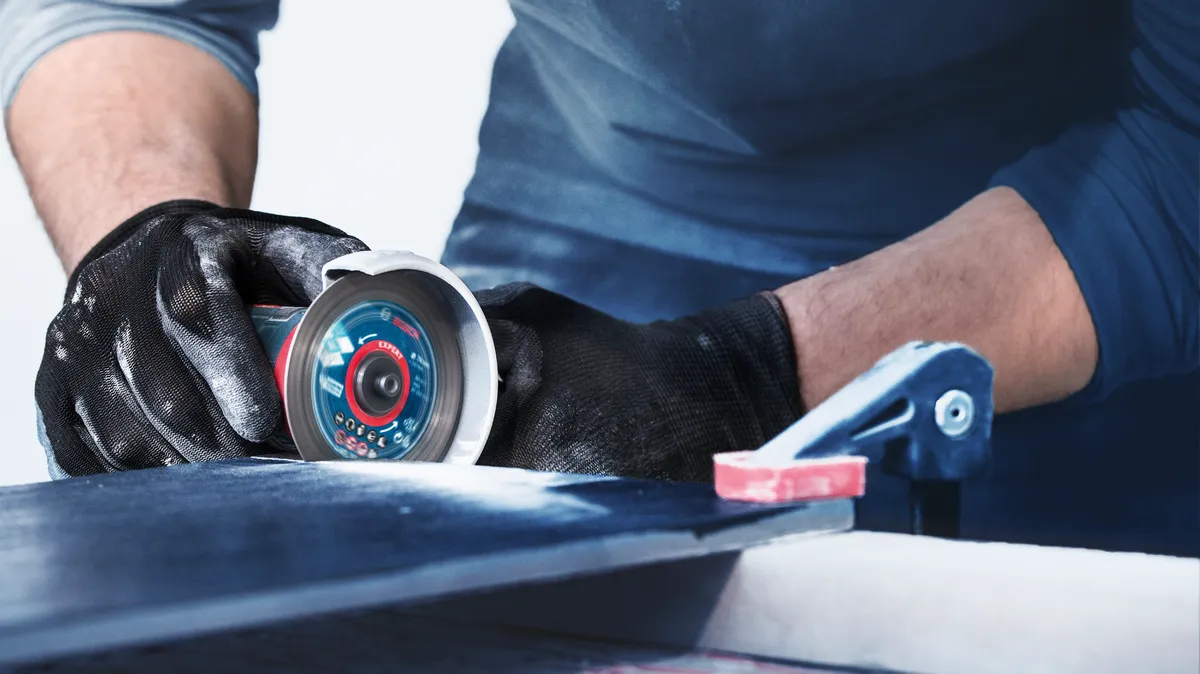 Persoon met veiligheidsuitrusting snijdt tegels met een elektrisch gereedschap.