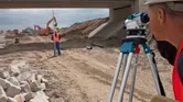Een persoon die veiligheidsuitrusting draagt, gebruikt een waterpas op een bouwplaats.
