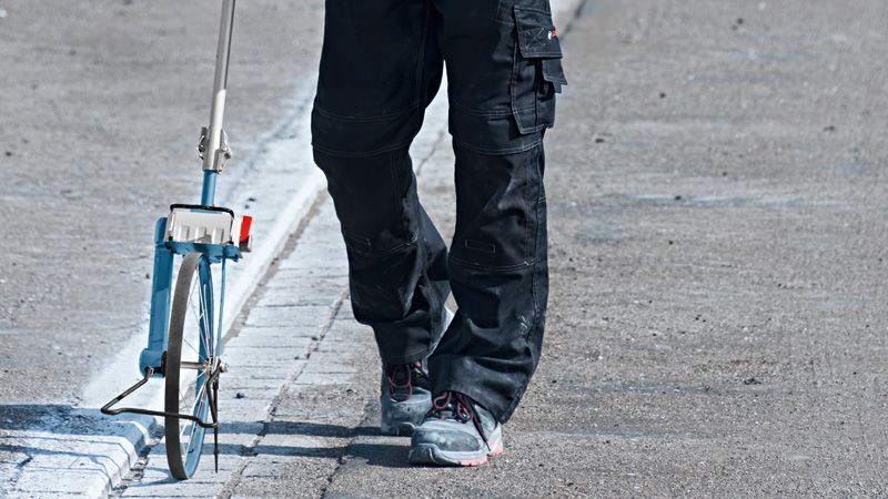 Een persoon die veiligheidsuitrusting draagt, meet de afstand over de weg met een meetwiel.