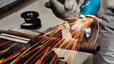 Een persoon met veiligheidsuitrusting slijpt een verroeste metalen pijp met een haakse slijper.