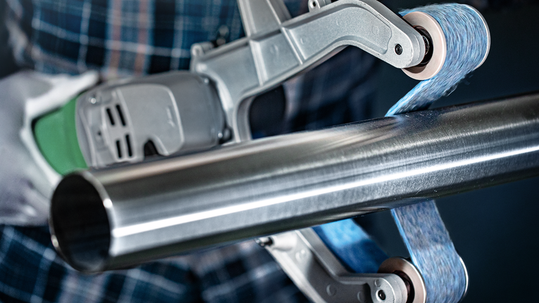 Een persoon die veiligheidsuitrusting draagt, polijst een metalen pijp met een elektrisch gereedschap.