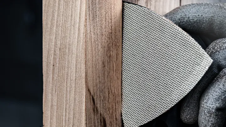 Een persoon die veiligheidsuitrusting draagt, schuurt een houten oppervlak met een schuurgaas.