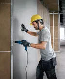 Een persoon met veiligheidsuitrusting boort in gipsplaat in een gebouw in aanbouw.