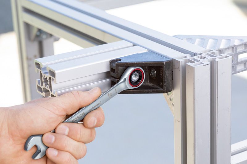 Iemand draait een bout op een metalen frame vast met een combinatiesleutel.