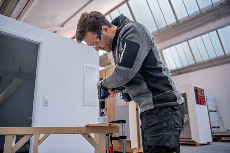 Een persoon die veiligheidsuitrusting draagt, boort een gat in hout met behulp van een snoerloze boormachine.