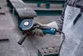 Een persoon die veiligheidsuitrusting draagt, houdt een haakse slijper vast in een industriële omgeving.