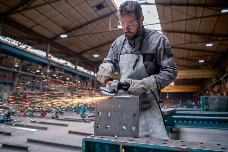 Een persoon die veiligheidsuitrusting draagt, slijpt een metalen blok met een haakse slijper, waarbij vonken ontstaan.