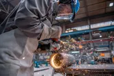 Een persoon met veiligheidsuitrusting slijpt een metalen pijp met een haakse slijper.