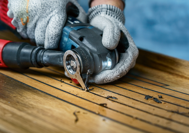 Een persoon die veiligheidsuitrusting draagt, gebruikt een multitool om houten vloeren te zagen.