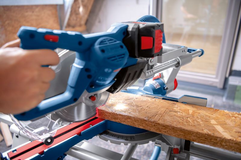 Iemand gebruikt een snoerloze verstekzaag om een ​​houten plank door te zagen.