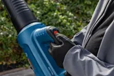 Een persoon die veiligheidsuitrusting draagt, bedient een snoerloze bladblazer buitenshuis.