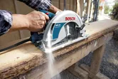 Een persoon zaagt een houten plank met een handcirkelzaag op een werkbank.
