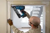 Een persoon die veiligheidsuitrusting draagt, gebruikt een snoerloze afwerknageltang op een deurkozijn.