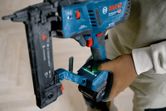 Persoon met veiligheidsuitrusting die een snoerloze smalle kroonnietmachine gebruikt.