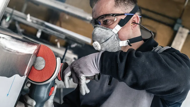 Een persoon die veiligheidsuitrusting draagt, polijst metaal met een elektrisch gereedschap.