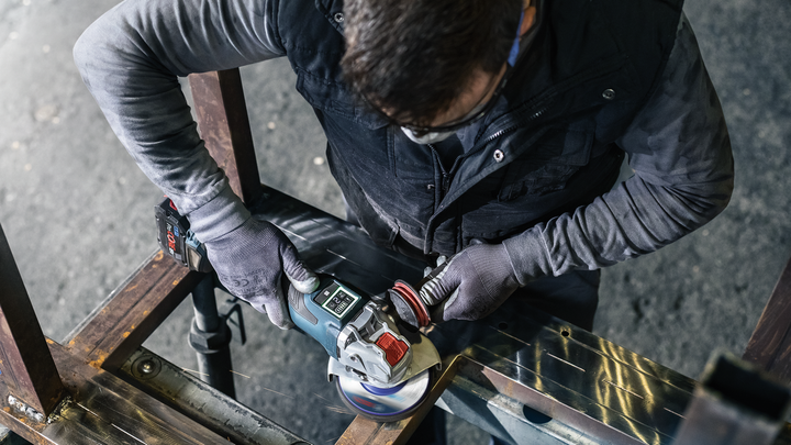 Persoon die veiligheidsuitrusting draagt, slijpt een metalen balk met een haakse slijper.