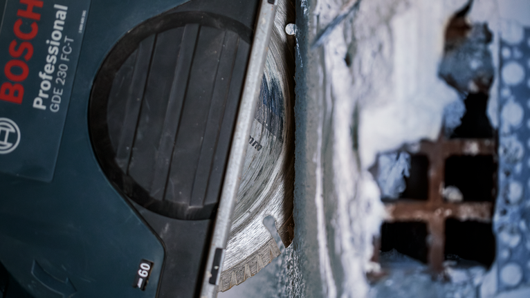 Diamantzaagblad zaagt door beton vlakbij een metalen rooster.