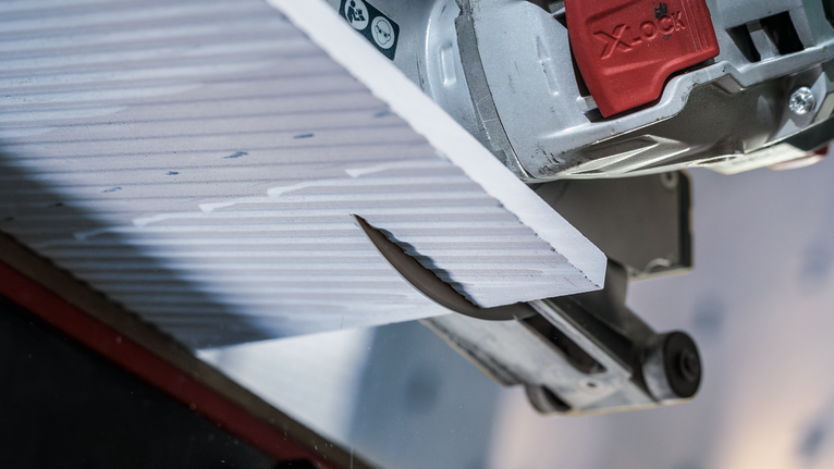 Een cirkelzaag zaagt een structuurtegelpaneel in close-up.