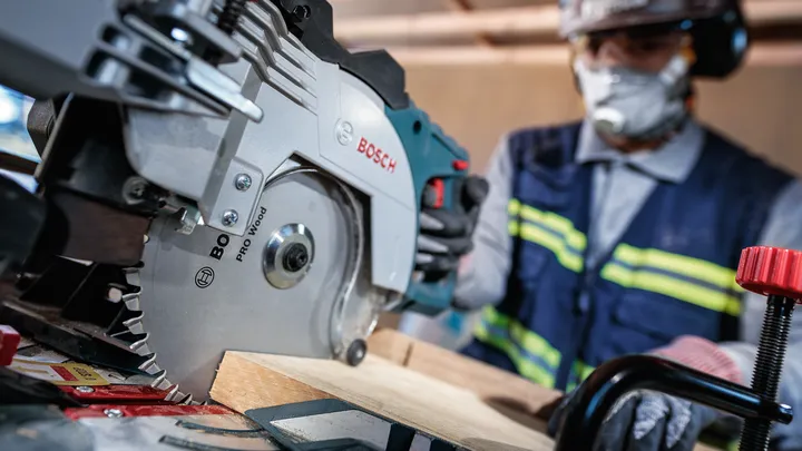 Een persoon die veiligheidsuitrusting draagt, gebruikt een cirkelzaag om houten planken te zagen.