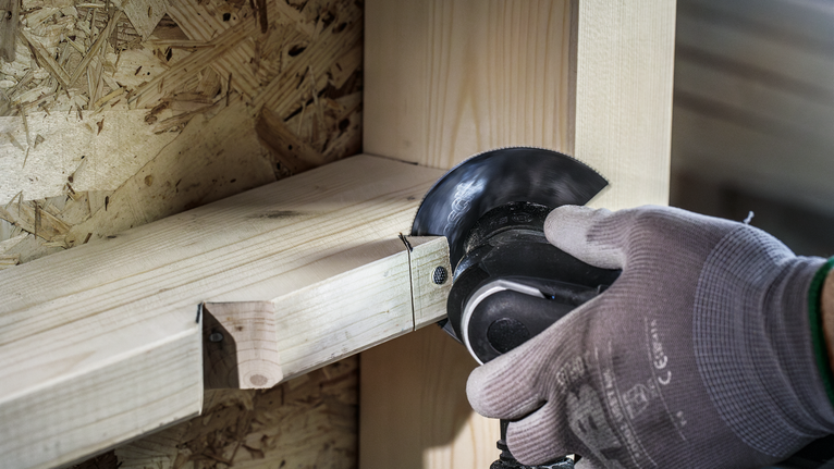 Persoon met veiligheidsuitrusting zaagt houten balken met een haakse slijper.