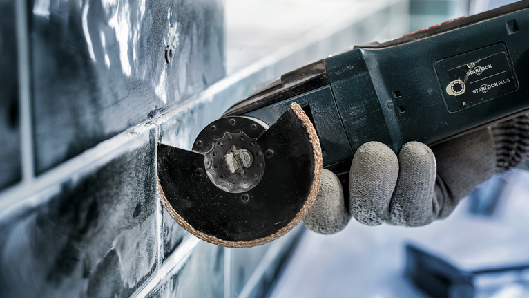 Een persoon die veiligheidsuitrusting draagt, gebruikt een elektrisch gereedschap om tegels te snijden.