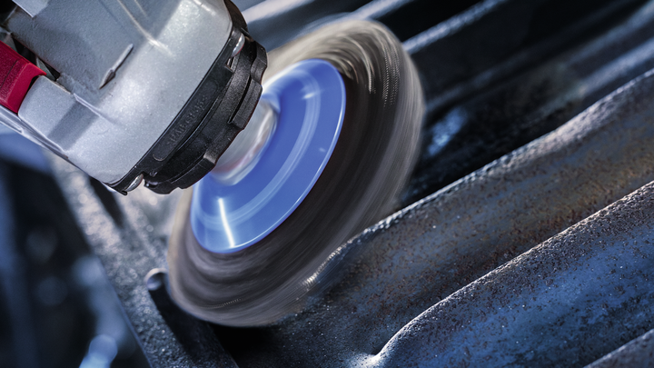 Roterend gereedschap met een staalborstelopzetstuk verwijdert roest van gegroefde metalen oppervlakken.